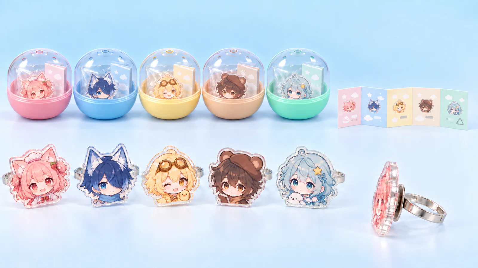 背の低い透明ドーム上蓋と浅いカラー下蓋を組み合わせた5色の丸型カプセルに5柄のアクリル印刷リングを封入し、文字を目立たせない図案中心の説明紙を添えた混装例